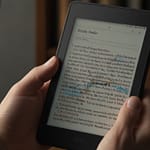 Kindle Paperwhite e-reader showing paper-like e-ink display with front lighting and extensive digital book library access