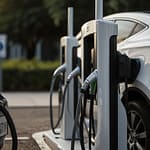Urban landscape with sleek electric vehicle charging stations featuring solar panels and digital displays showing charging status in a modern city setting
